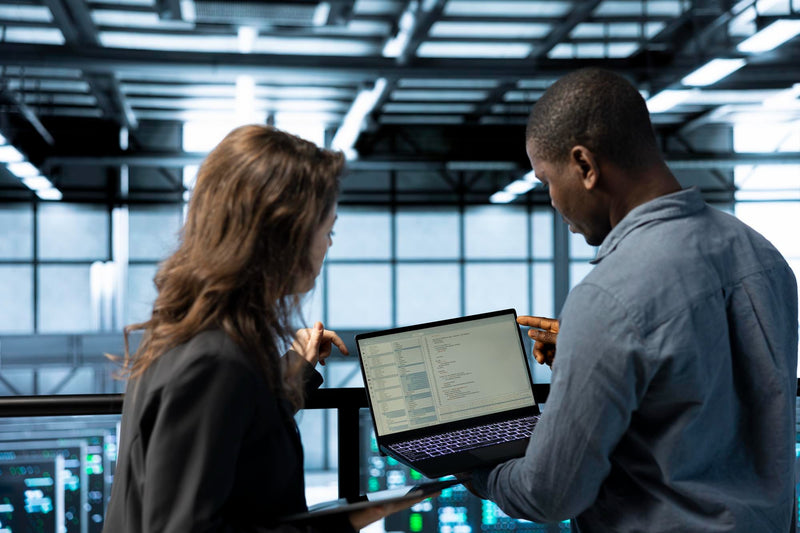 A commercial finance broker reviewing data verification checklists and business records on a laptop screen in a modern office workspace.