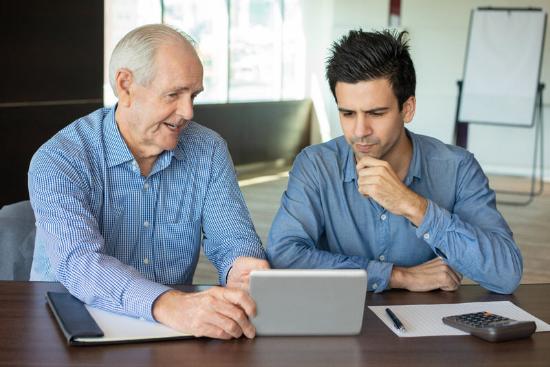 A senior funding broker demonstrating business loan options on a digital tablet to a pensive business owner looking to secure working capital.