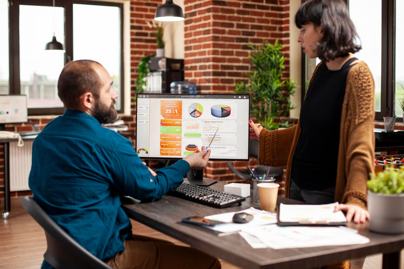 Two ISO marketing specialists reviewing automated campaign analytics and MCA renewal leads performance metrics on a desktop monitor.