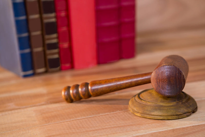 A close-up of a wooden judge's gavel on a desk with law books blurred in the background, representing state-by-state merchant cash advance disclosure regulations and legal compliance trackers.